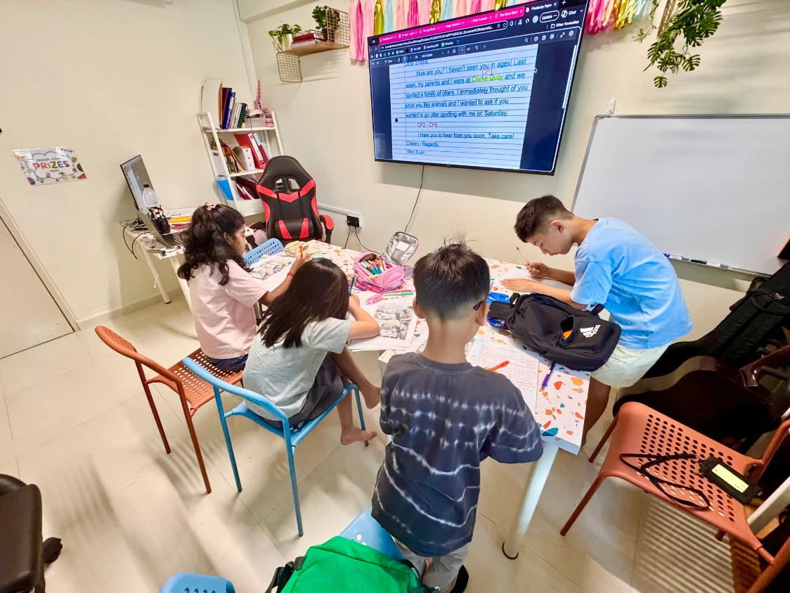 Students writing together at a table in the Happy Quills classroom